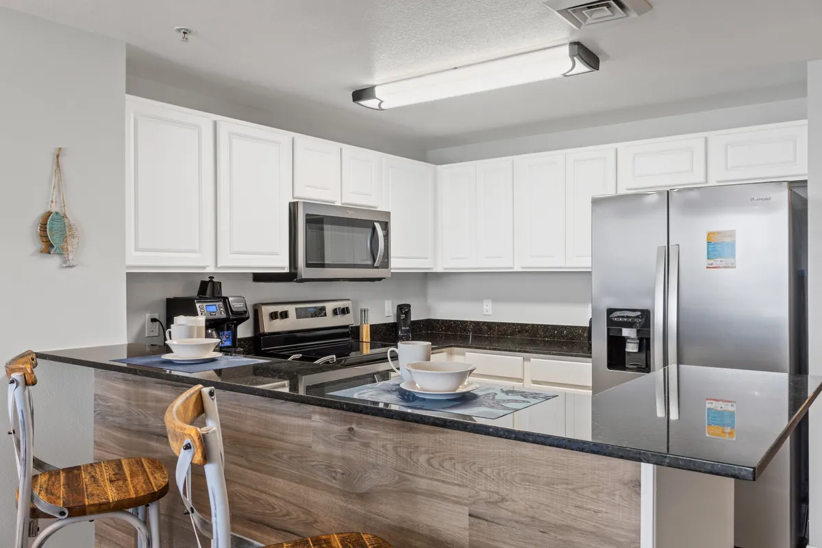 A modern kitchen with ample countertop space, stainless steel appliances, and bar stools lined up along the counter. The scene is bright, well-organized, and highlights the functionality and social aspect of the kitchen, making it ideal for both cooking and casual gathering.