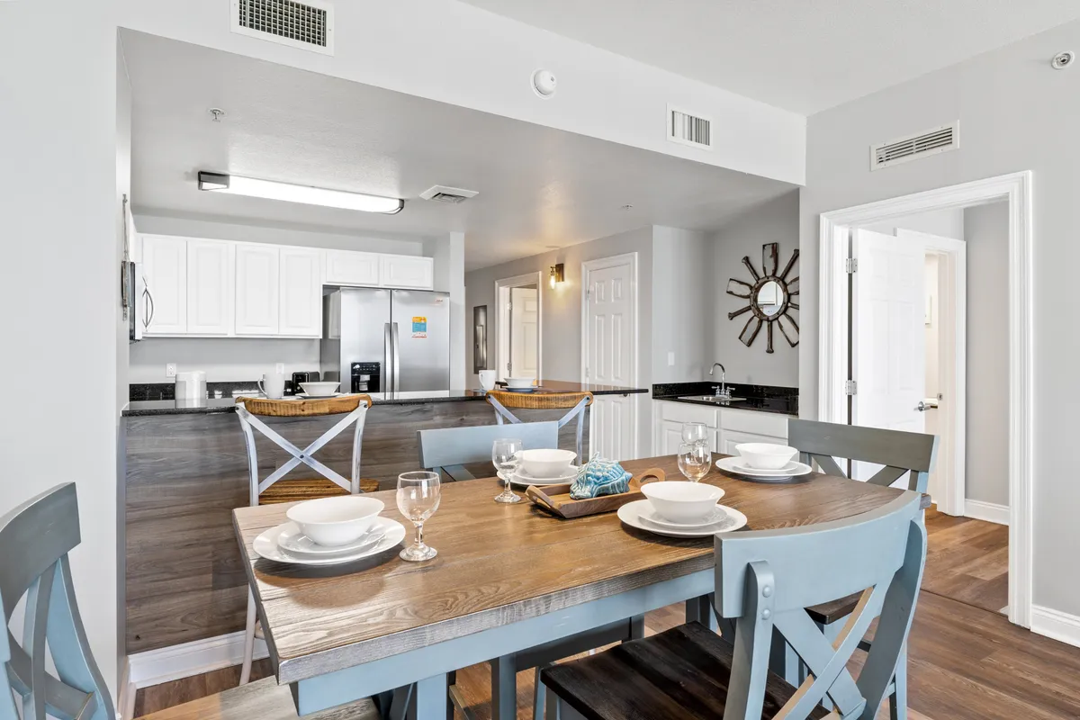 A dining table set for a meal is positioned adjacent to the kitchen, with place settings ready for family or guests. Stainless steel appliances and a decorative mirror add a touch of elegance, while the open layout fosters a communal, welcoming atmosphere.