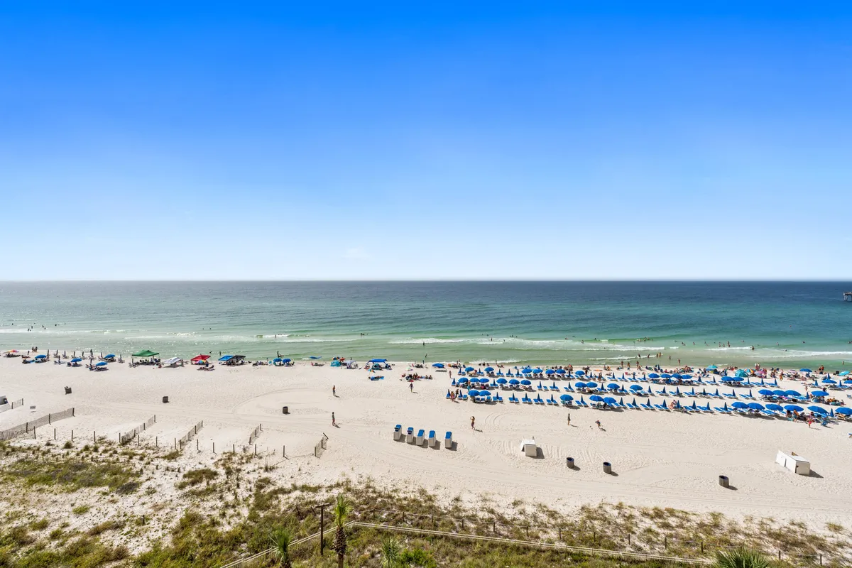 A vibrant scene of a sunlit beach with soft sand, gentle waves, colorful beach chairs and umbrellas, and people enjoying various beach activities. The ocean stretches into the horizon, evoking a lively, summery atmosphere.