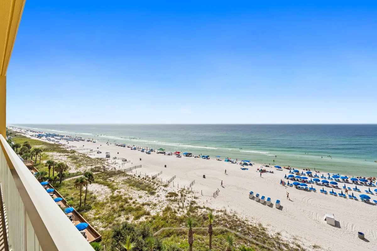 This scene highlights a pristine sandy beach lined with beach chairs and umbrellas, bordered by palm trees and gentle ocean waves. The mood is quintessentially vacation-like, with people sunbathing, swimming, and enjoying the shoreline under the Florida sunshine. The setting evokes relaxation and the spirit of coastal leisure.