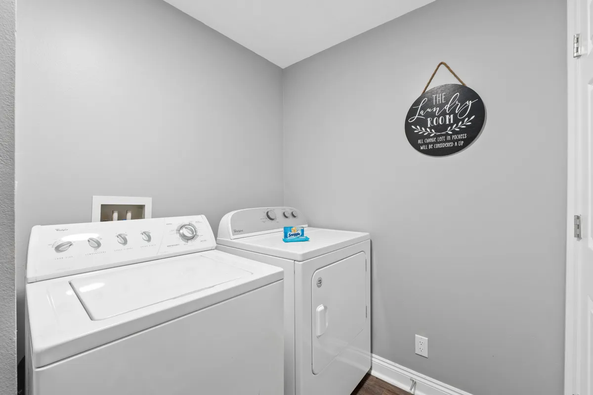 A practical laundry area with a white washing machine and dryer, laundry soap on top, and a decorative wall sign. The space is neat and modern, providing essential convenience for longer stays or families.