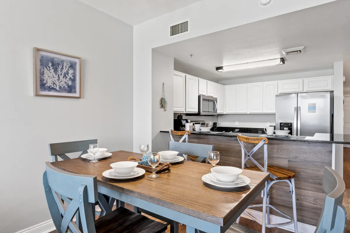 A dining space with a wooden table set for four, a kitchen countertop with bar stools, stainless steel appliances, and white cabinetry. The setting is modern and welcoming, ideal for family meals or casual gatherings before or after exploring nearby attractions.